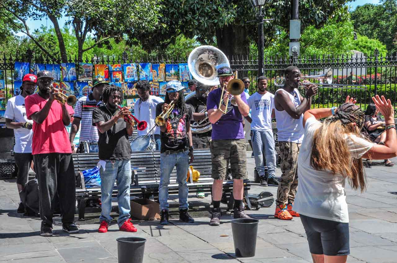A group of young men playing musical instruments together in a public place. a lady is dancing to the music