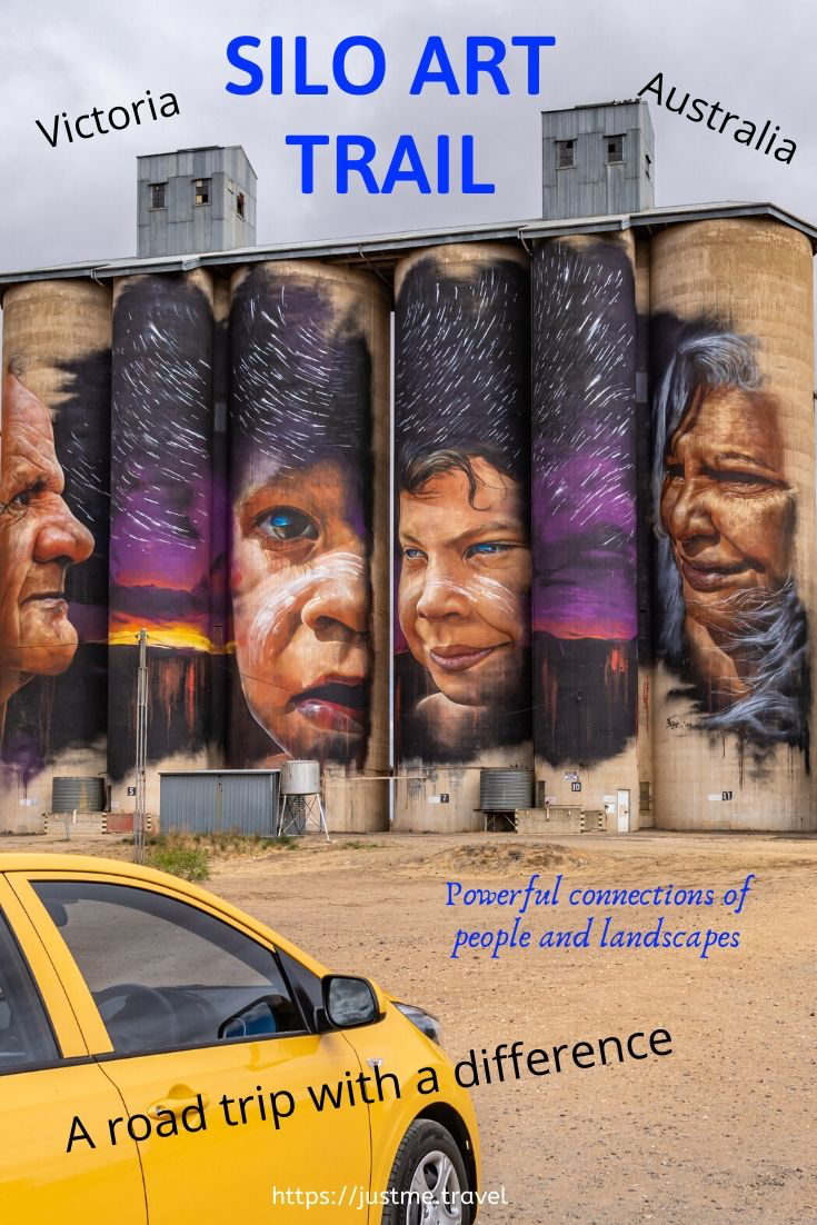 Aboriginal man, woman and two children painted on grain storage silos. a yellow car is in front of the silos.