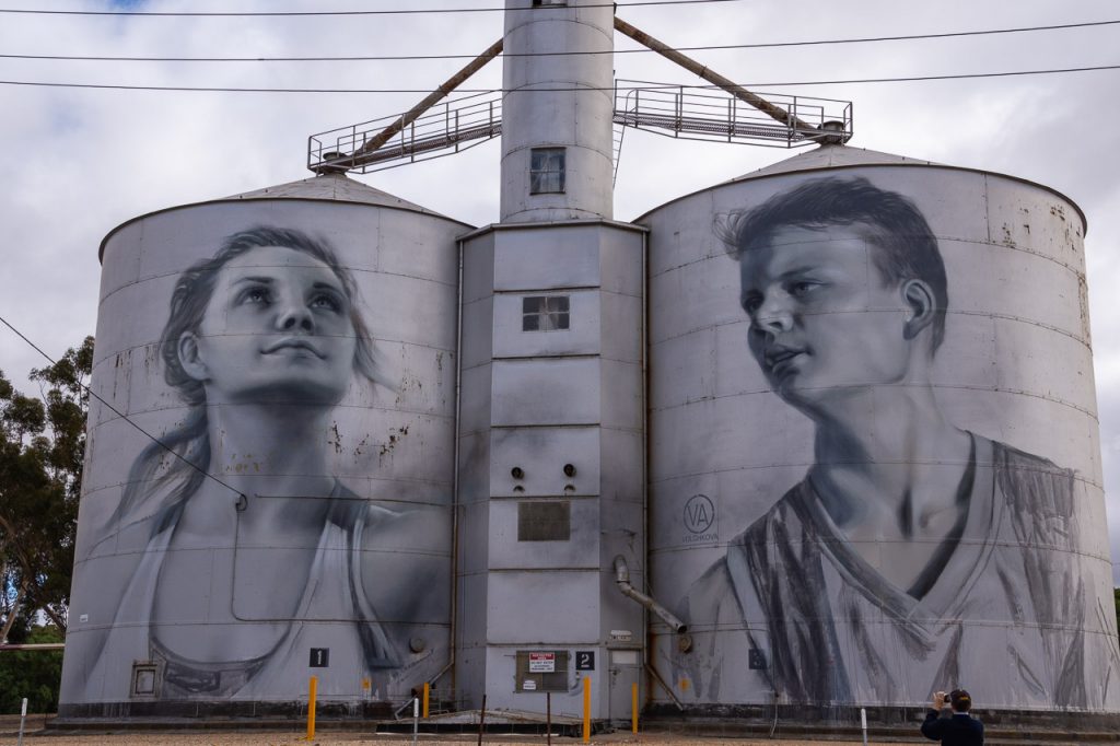 Black & white painting of a girl and a boy in team uniforms on metal grain silos