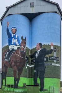 Painting on silos of a jockey on a horse with the training standing next to the horse