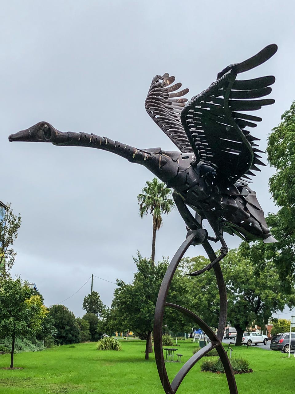 A sculpture in a park of a black swan made from recycled metal