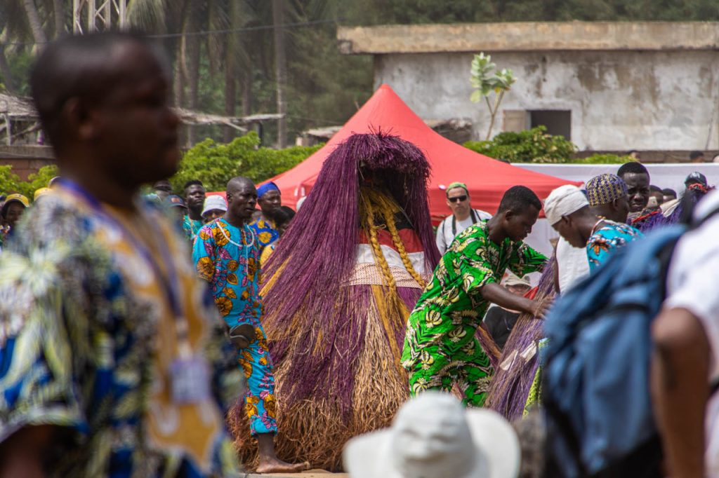 A person covered in purple and yellow straw, dressed as the Voodoo spirit known as Zangbeto