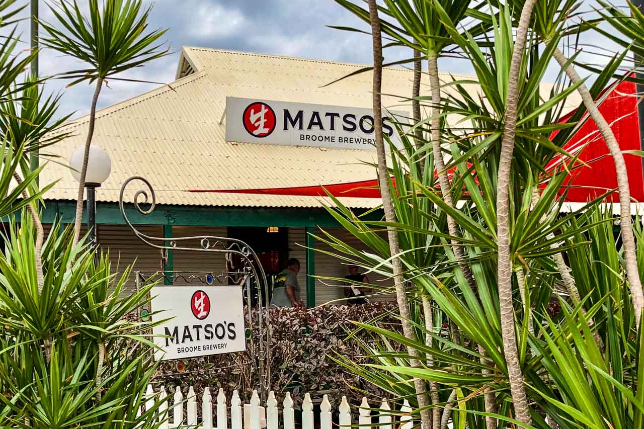 A house surrounded by palm trees. The sign on the roof of the house and hanging on the fence reads "Matso's Broome Brewery"