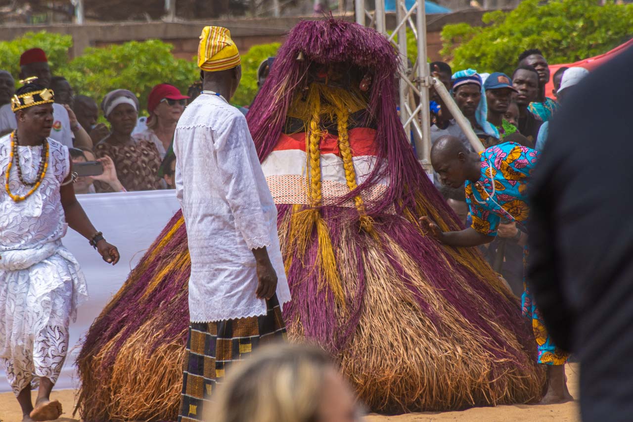A person covered in purple and yellow straw, dressed as the Voodoo spirit known as Zangbeto