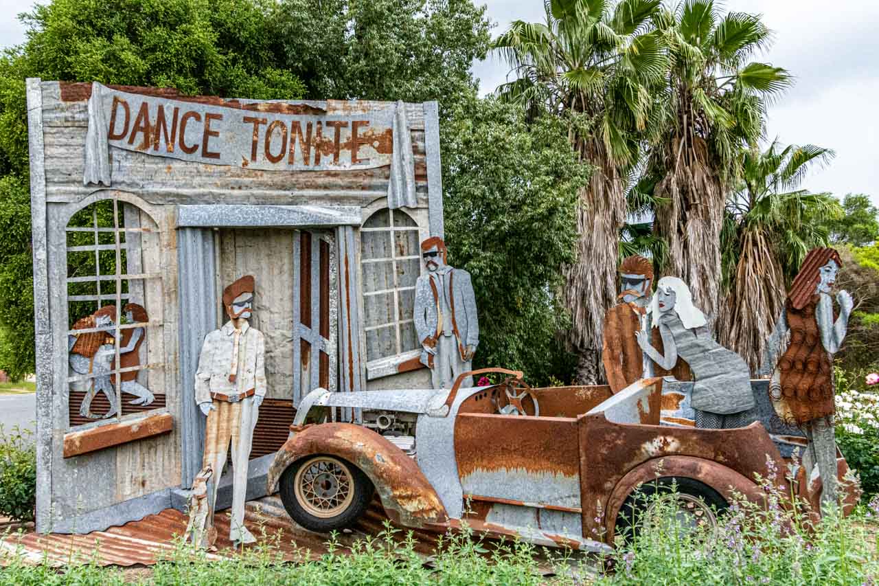 A rusty metal sculpture of a car and people outside a dance hall