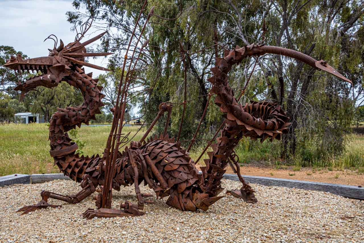 A rusty metal sculpture of a dragon made from recycled farm parts