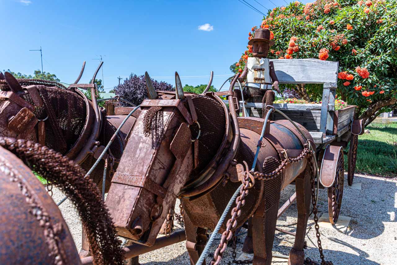 A rusty metal sculpture of a person driving a wagon pulled by horses