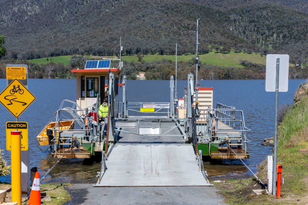 A cable three-car ferry prepares to cross a river. The Ferrymaster stands ready to open the ferry gate.