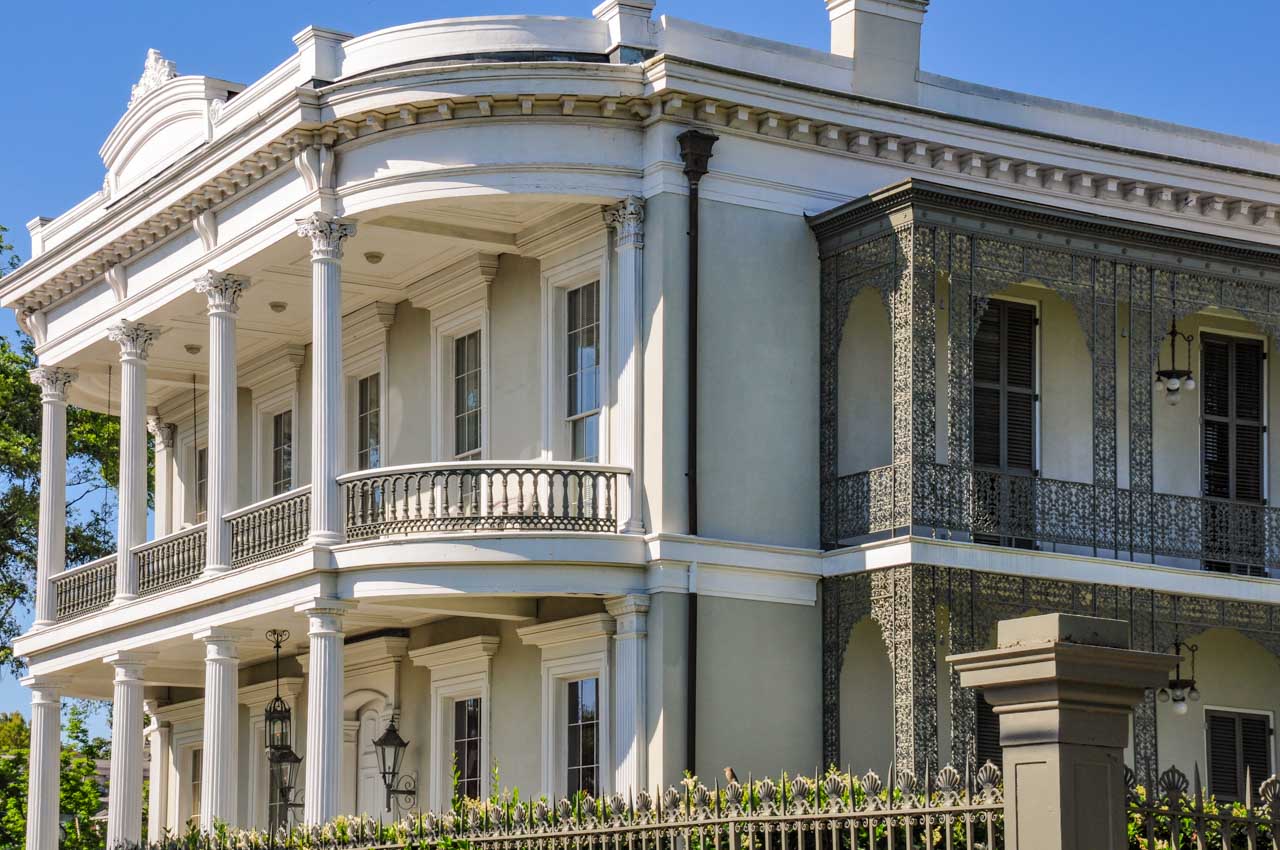 A to-story White House with columns on the front verandas and wrought-iron balconies on the side of the house.