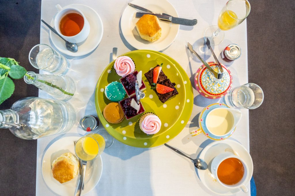 A table set with a plate of cakes, scones, cups of tea, orange juice, and water.