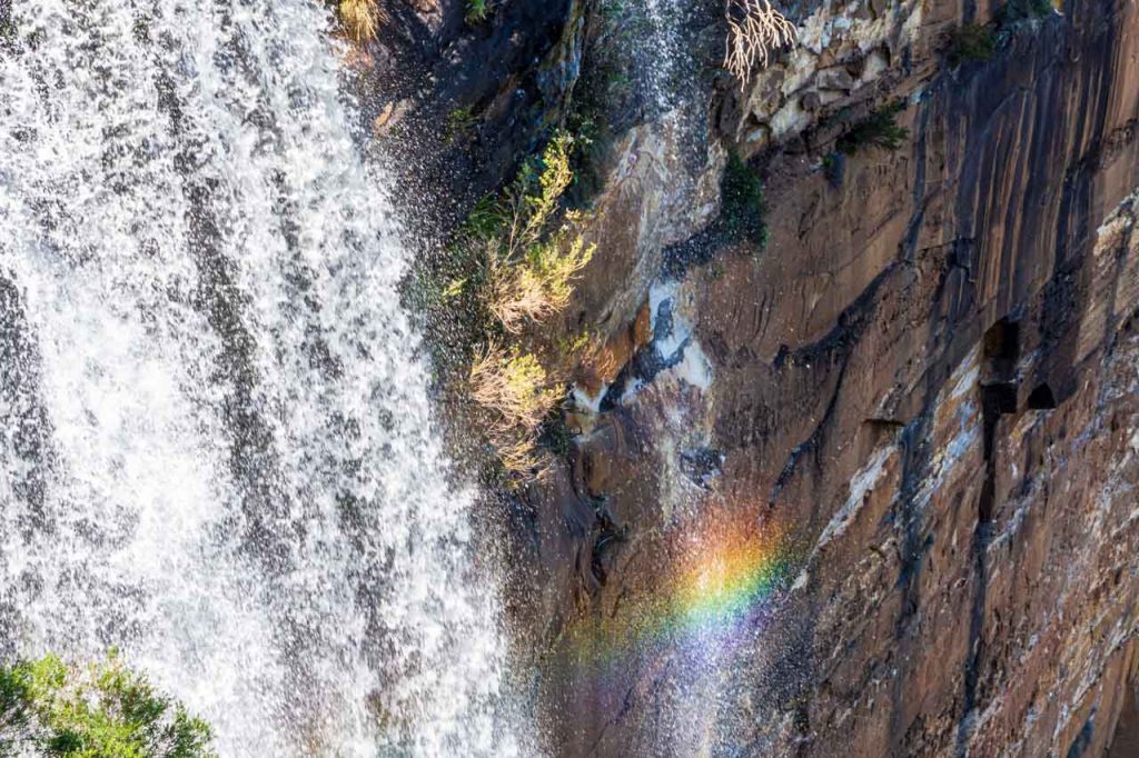 Photo of a waterfall with a rainbow reflected on the rock cliff face.