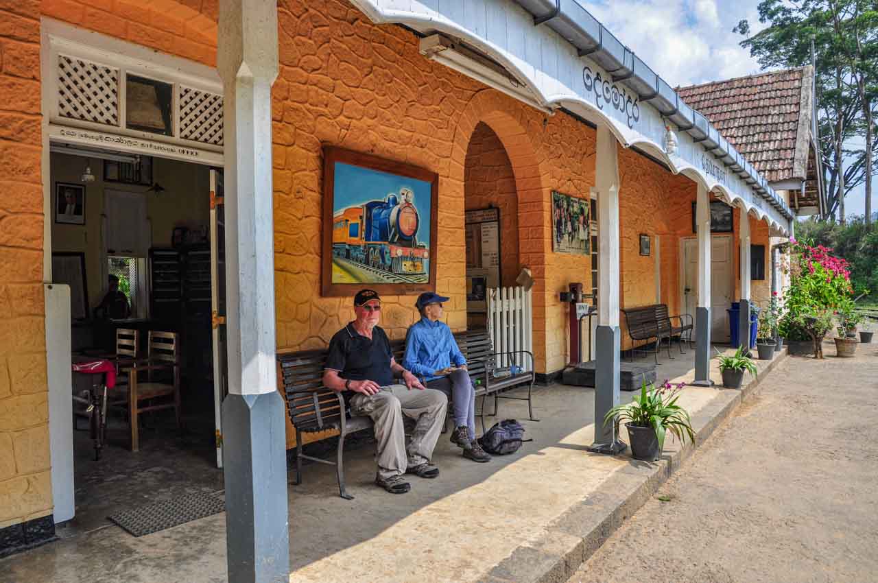 Two people sitting on a train platform underneath a picture of a steam train engine.