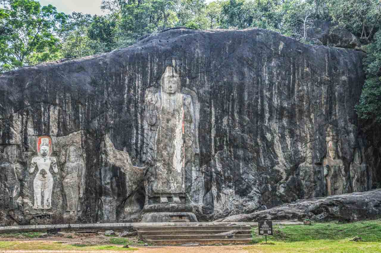 An image of Buddha and six other figures are carved into the rock face.