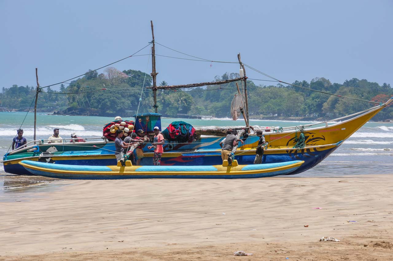 Several men push their large fishing boat out of the water and onto the beach.