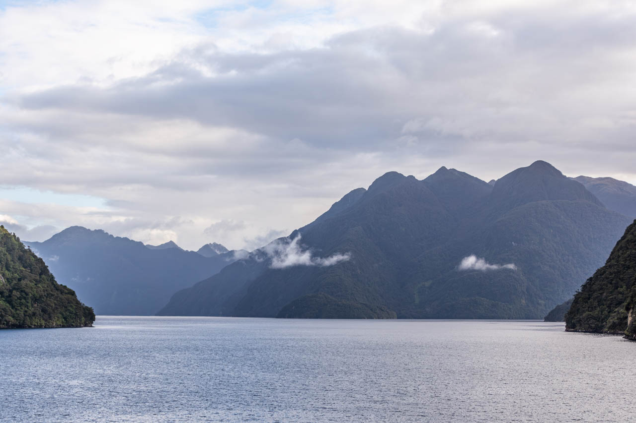 A body of water surrounded by mountains and low cloud cover.