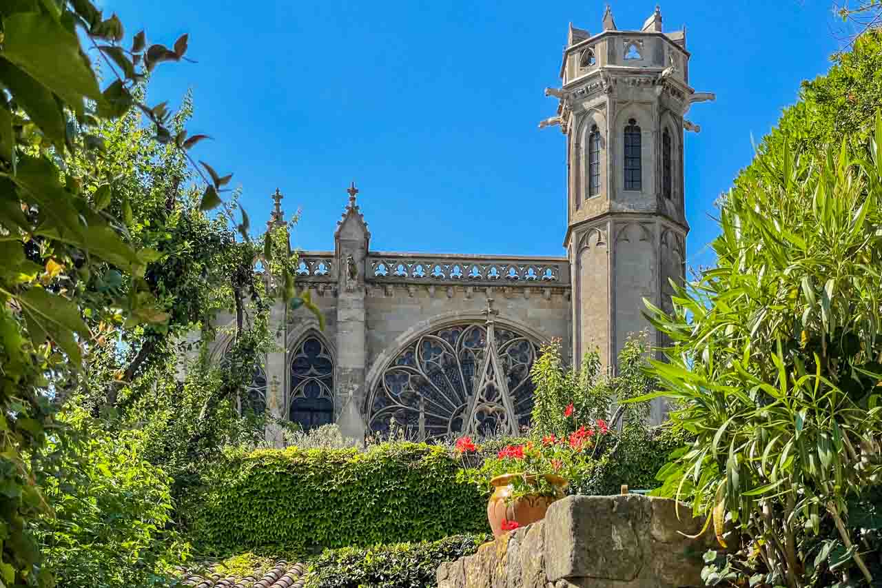 A gothic church facade with shrubs and flowers in front of it.