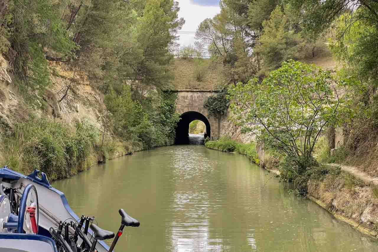 A boat approaches a tunnel in a hill with the canal passing through the tunnel.