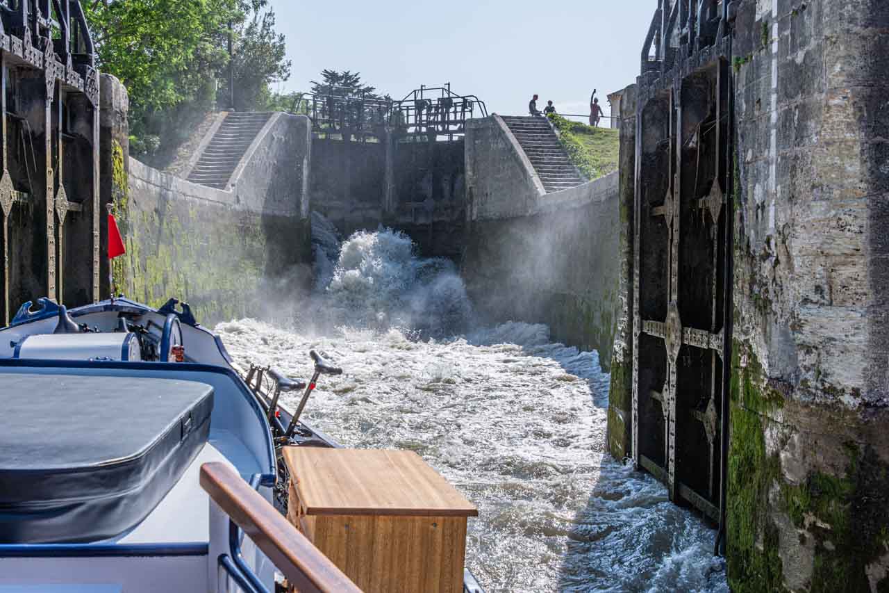 A boat moves into the rushing waters of a filling lock chamber.