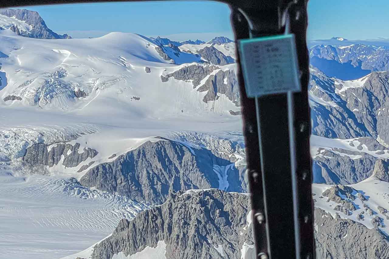 Snow covered mountains are viewed from inside a helicopter.