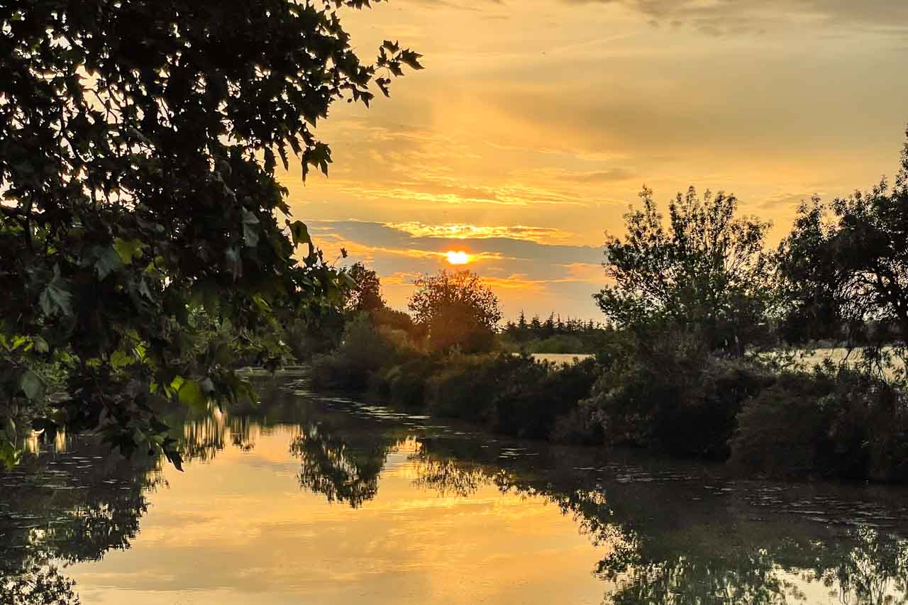 A sunset is reflected in the waters of a tree-lined canal.