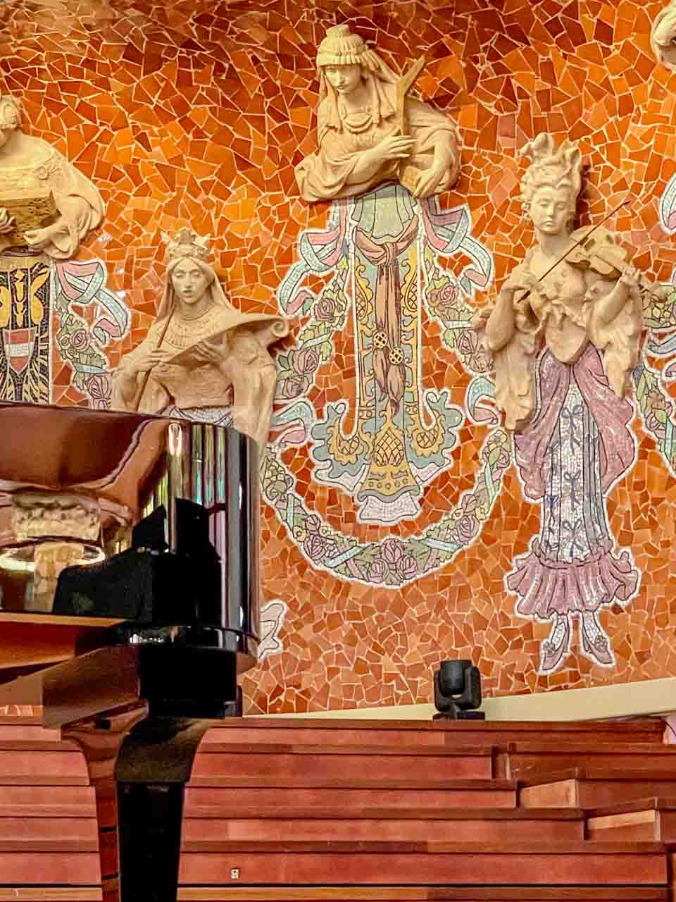 Sculpted ladies playing musical instruments are plastered on the wall behind a piano.