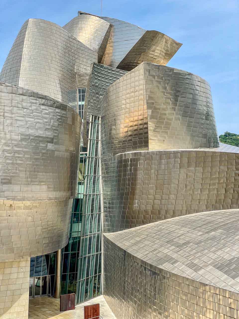 The silver-tiled and glass facade of the front of the Bilbao Guggenheim Museum.