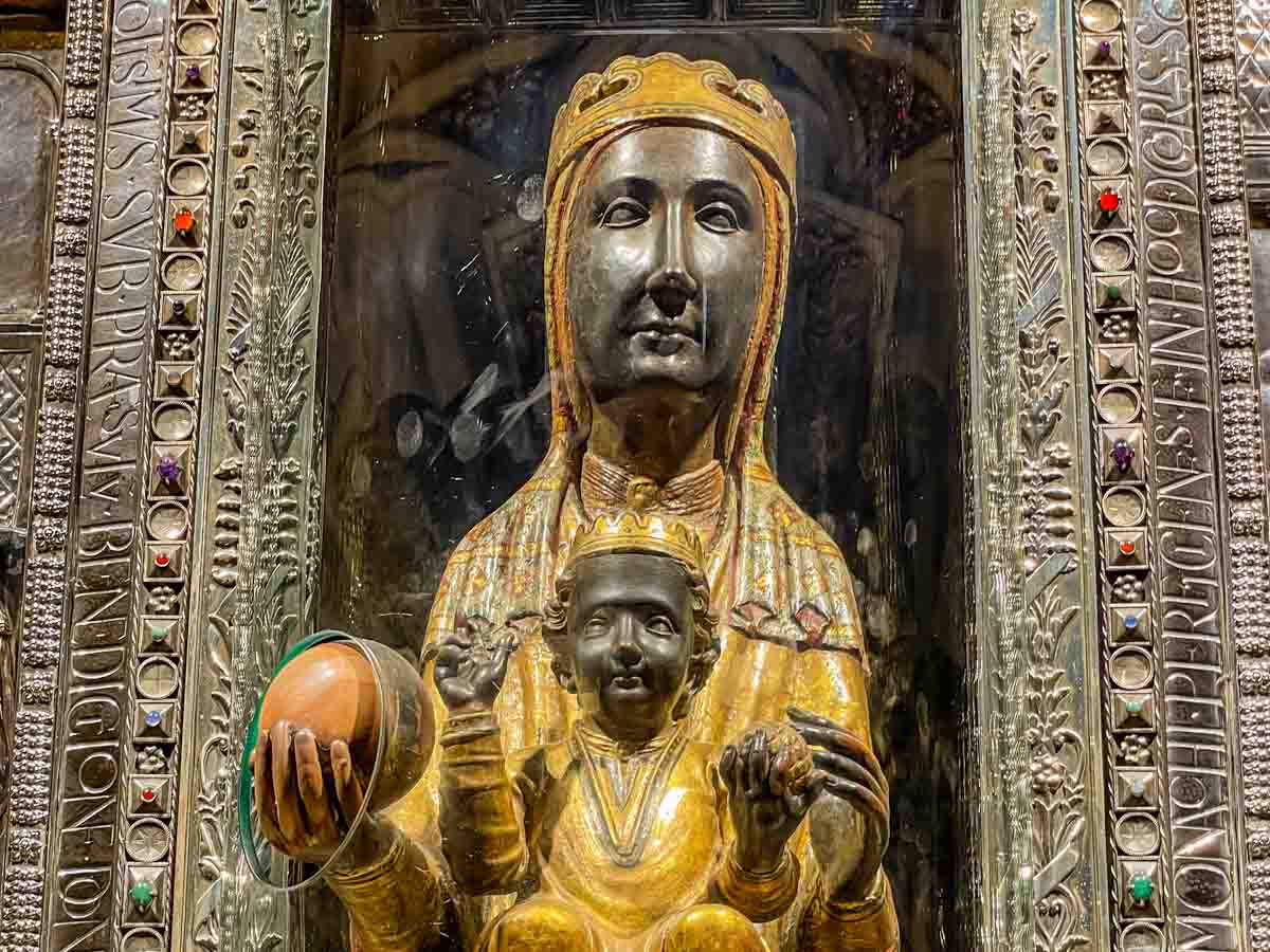A black madonna with baby Jesus sitting on her lap. She is holding a marble ball that people can rub. The figures are behind glass.