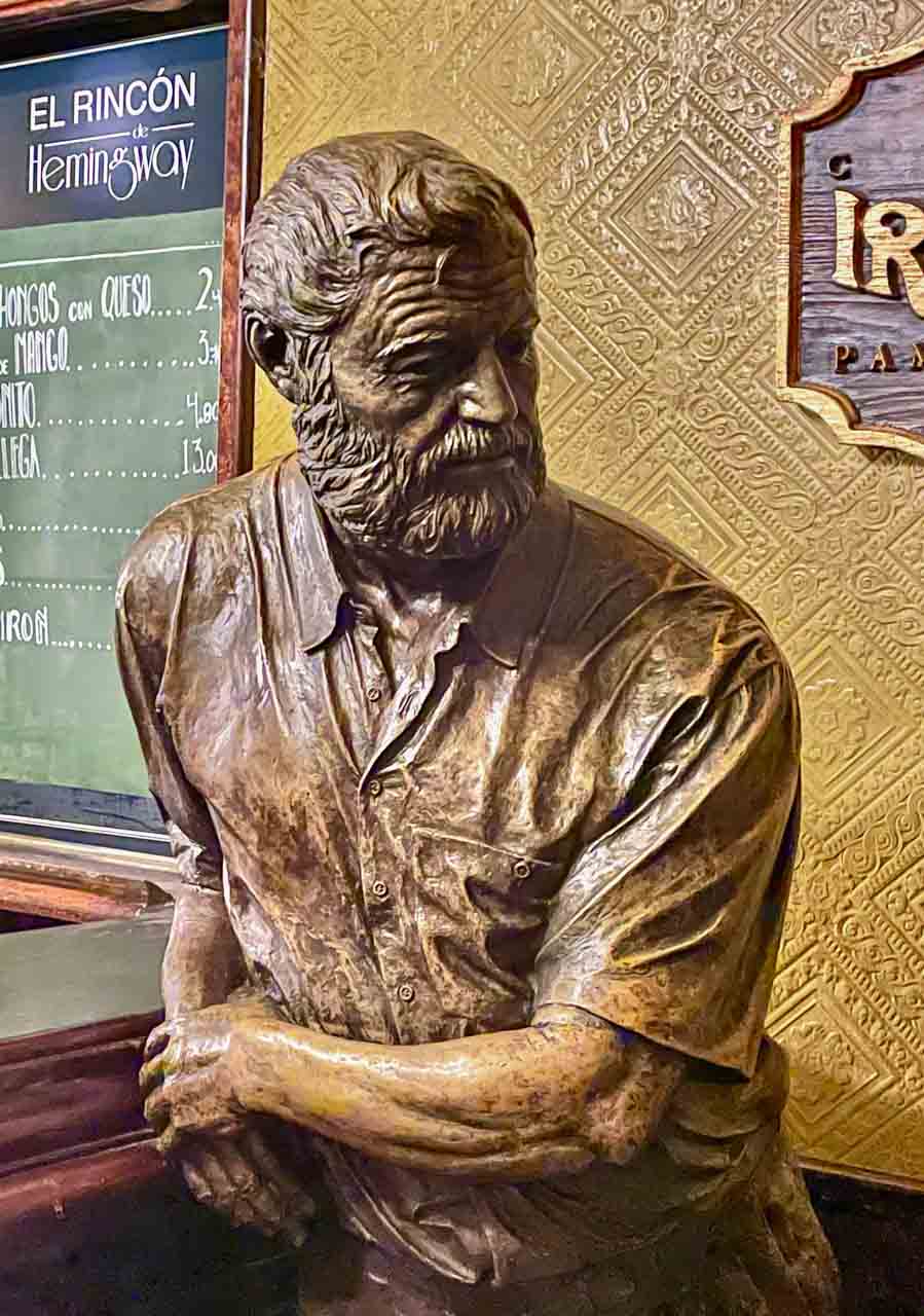 A bronze statue of the writer Ernest Hemingway leaning against a bar, with his right arm on the bar.
