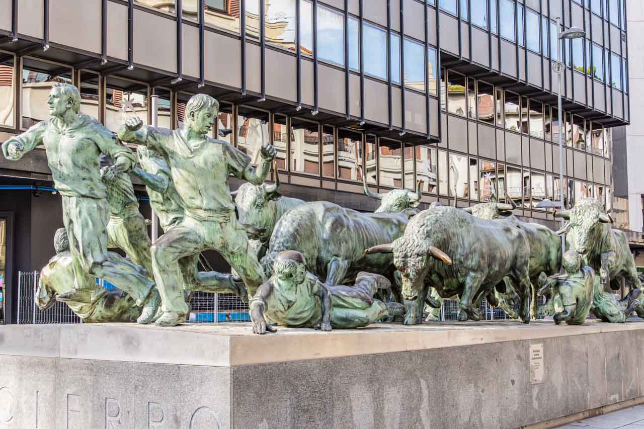 A metal monument of men running and lying on the ground with several bulls behind them.