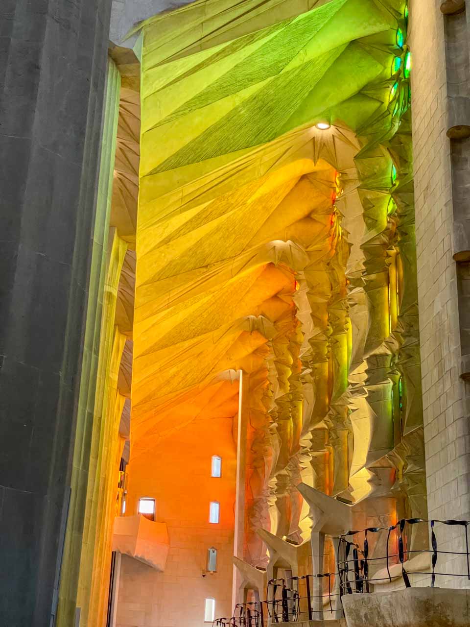 The light coming into the building from stained glass windows reflect orange, yellow, and green lights on the interior walls.