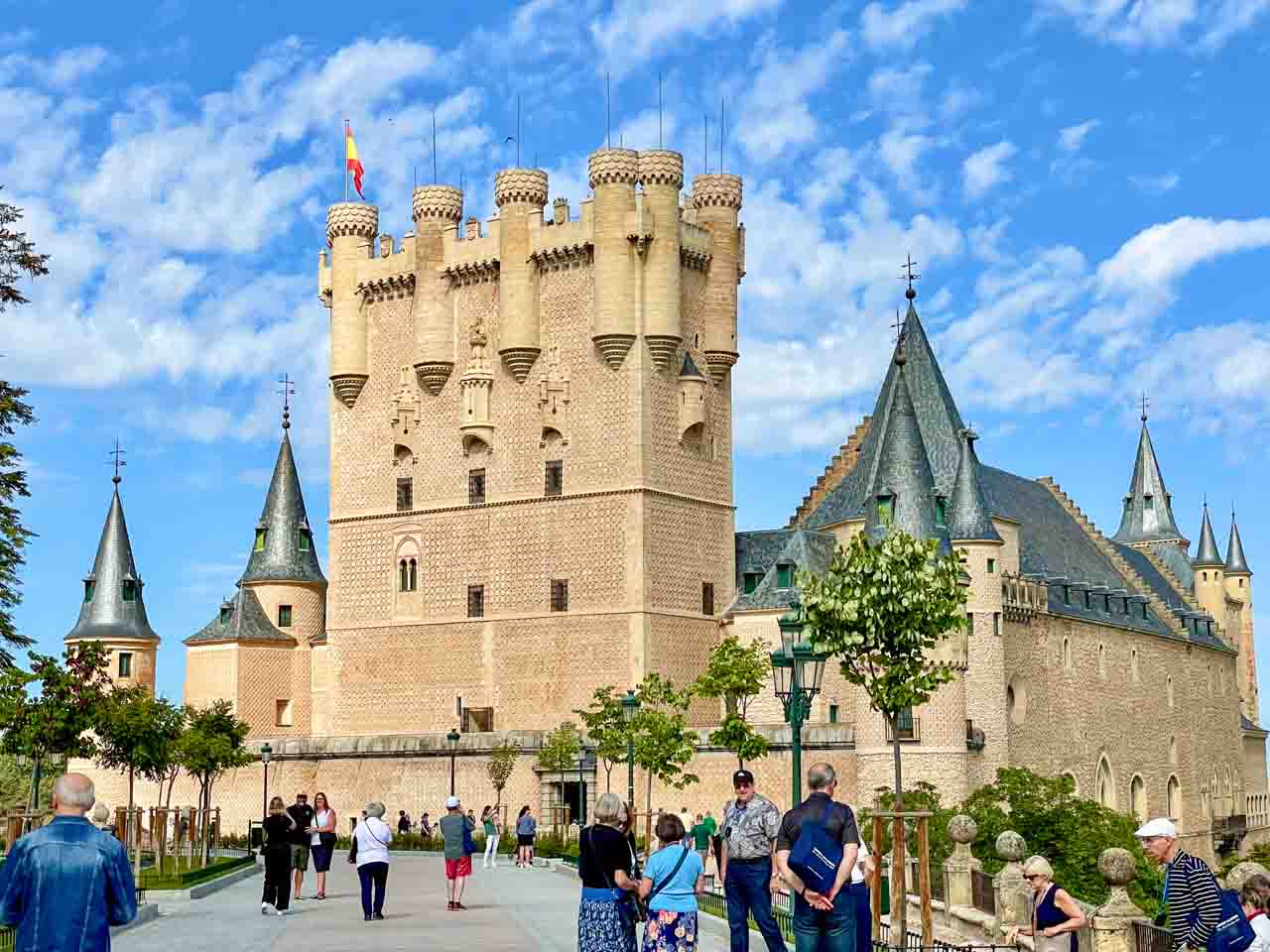 A castle with multiple turrets with tourists waiting to enter.