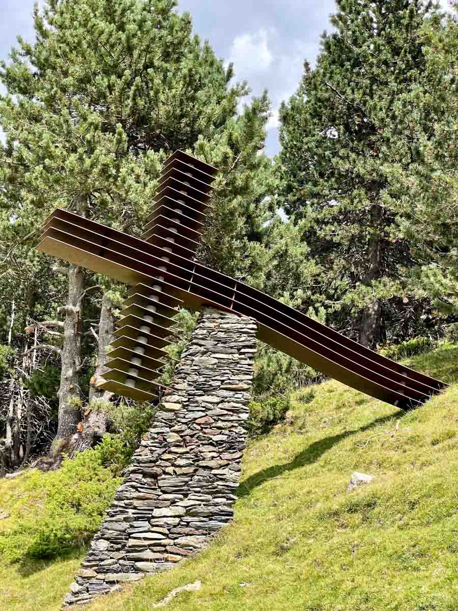 A metal cross supported by a stone pillar sits on the side of a hill.