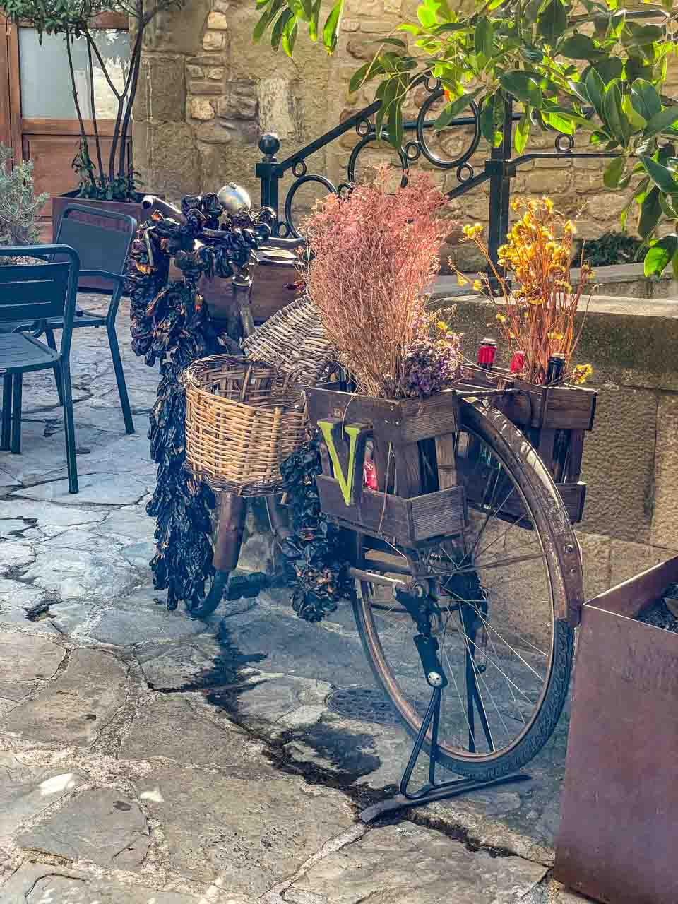 A bicycle adorned with wooden and wicker baskets sits an old town courtyard.