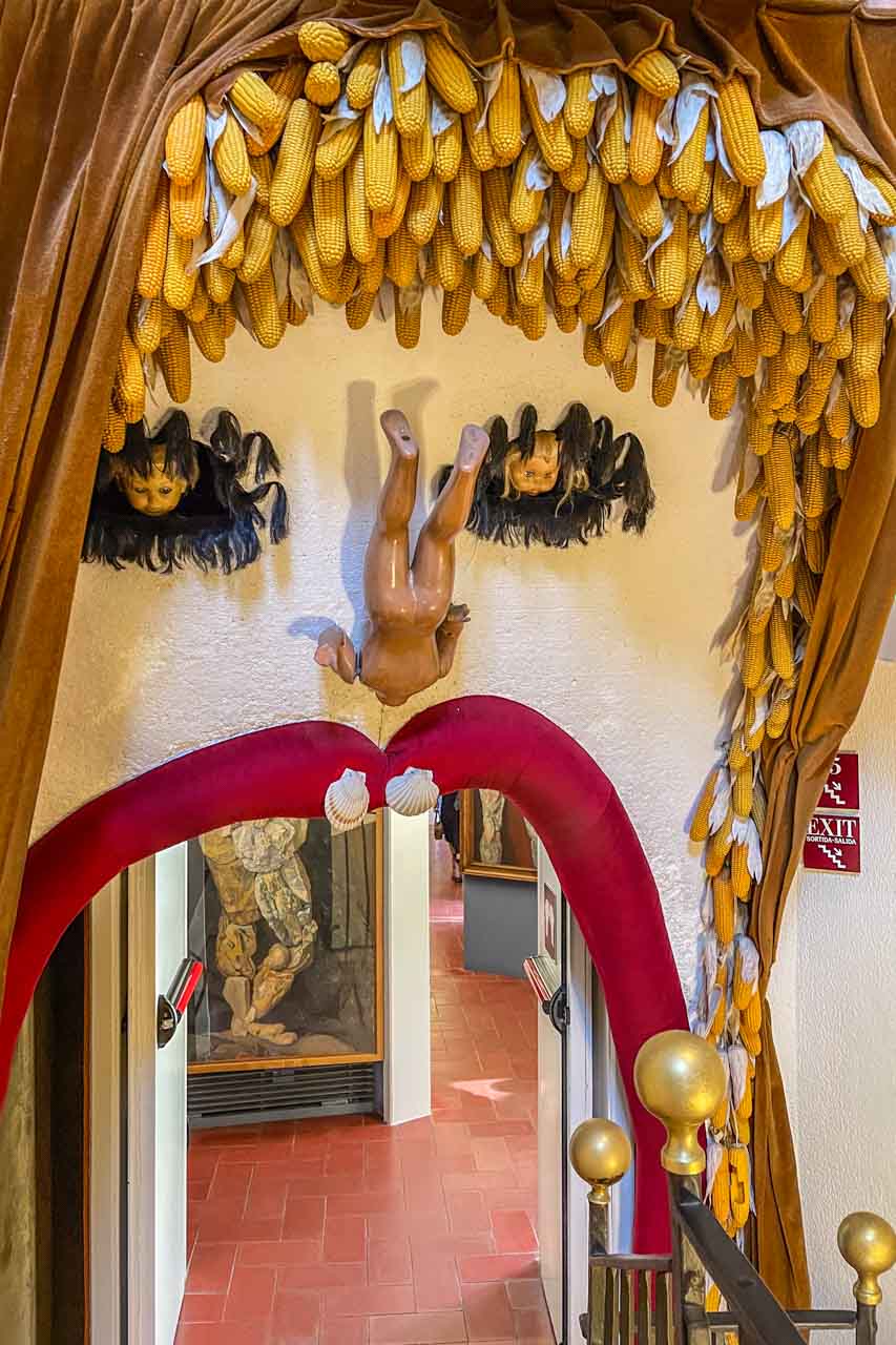 The interior of a museum decorated in a surrealist style with a doorway lined with red lips and corn cobs for hair.