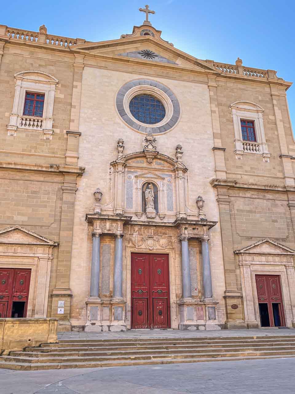 The stone front facade of a cathedral with red wooden doors.