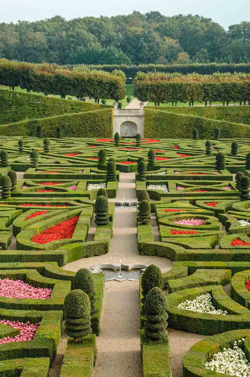 A formal garden with green hedges and pink, red, and white flowers.